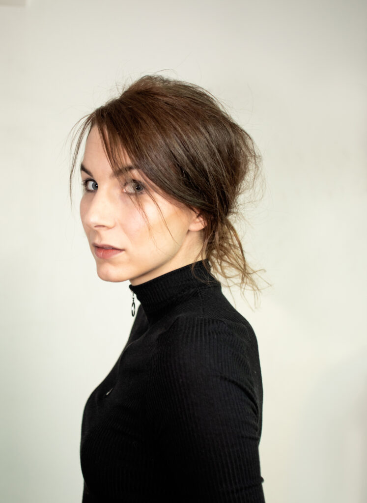 Portrait einer Frau mit schwarzem Obertteil vor einer Wand.